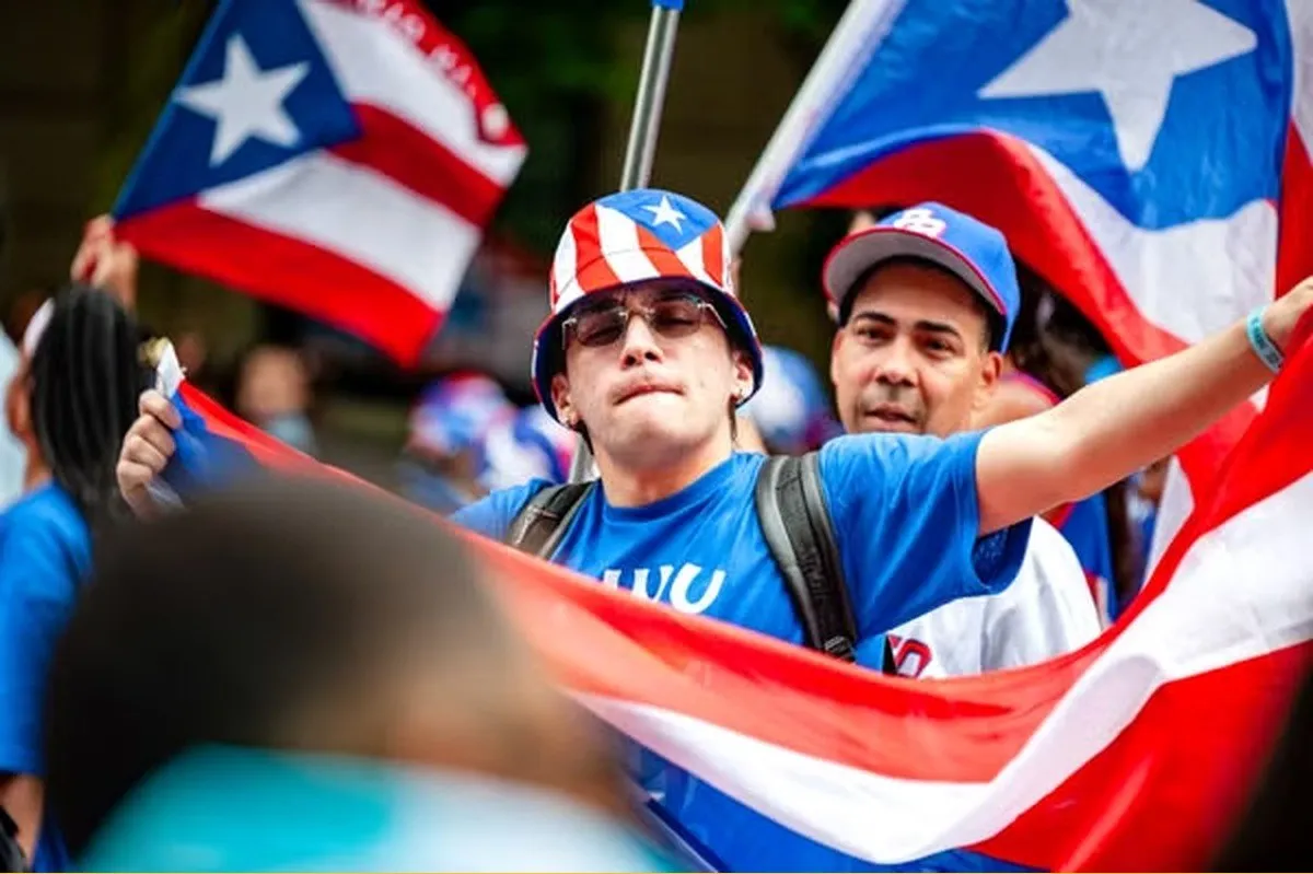 A young man in a Puerto Rican flag bucket hat holds a large flag at a parade in New York.